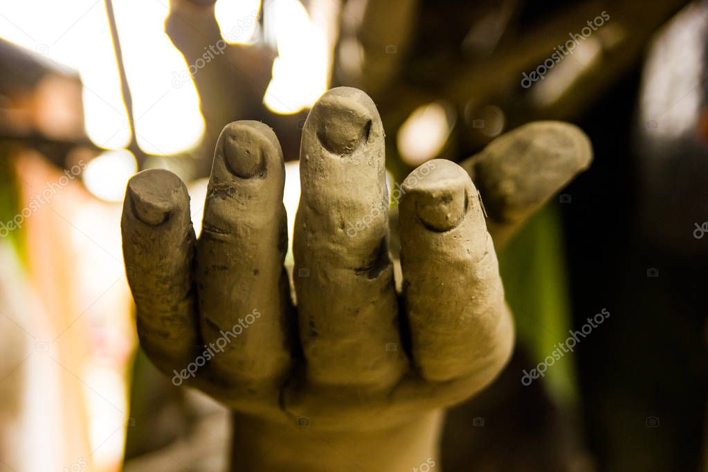 A hand of a statue made of clay under construction asking for help