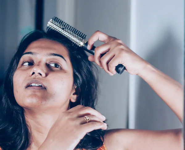 lady combing her hair with hairbrush at mirror.