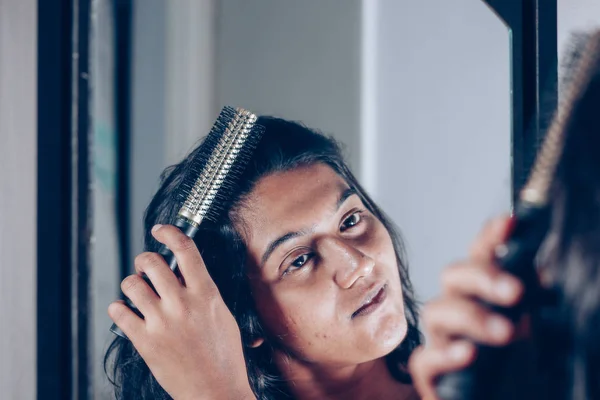 lady combing her hair with hairbrush at mirror.