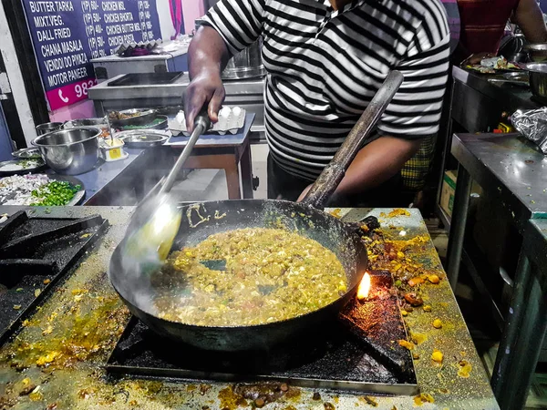 a chef cooking tadka fry in a frying pan at a road side food corner on a stove over flames