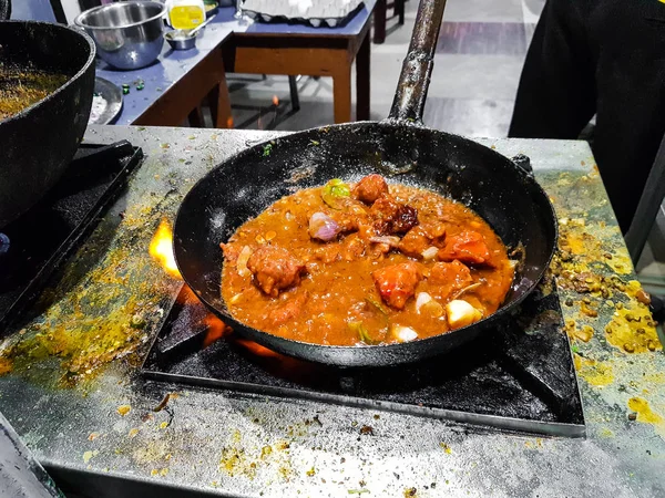 a chef cooking tadka fry in a frying pan at a road side food corner on a stove over flames