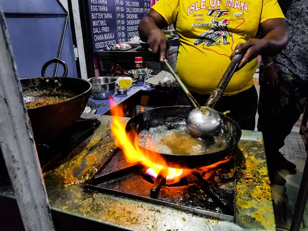 a chef cooking tadka fry in a frying pan at a road side food corner on a stove over flames