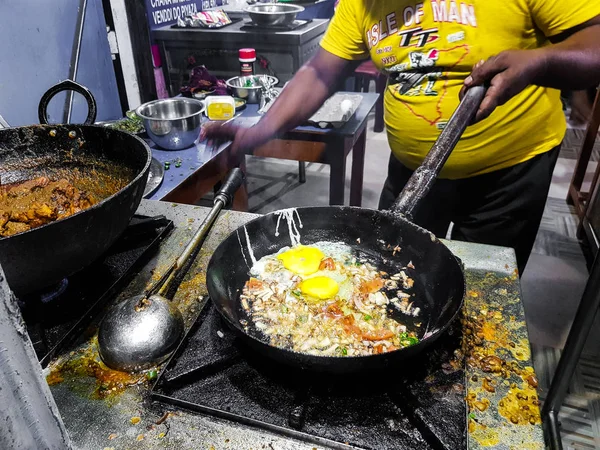 a chef cooking tadka fry in a frying pan at a road side food corner on a stove over flames