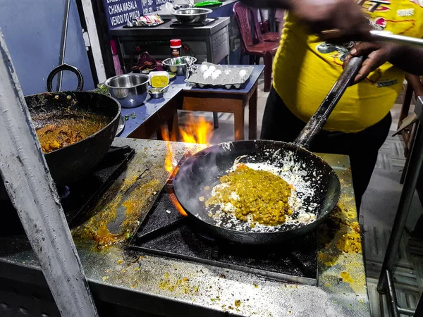 a chef cooking tadka fry in a frying pan at a road side food corner on a stove over flames