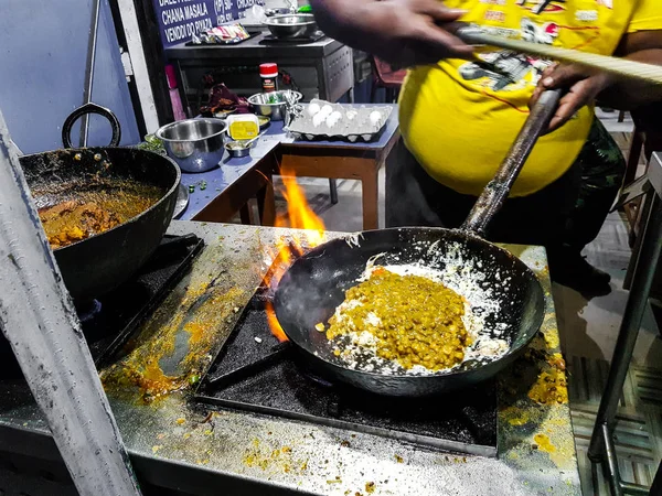 a chef cooking tadka fry in a frying pan at a road side food corner on a stove over flames