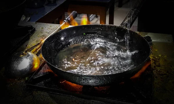 a chef cooking tadka fry in a frying pan at a road side food corner on a stove over flames