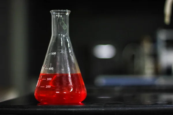 red liquid in a glass conical flask on a black granite table in dark background