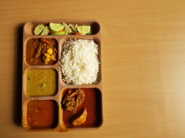 indian chicken thali with rice dal chicken salad vegetable curry on a plastic segmented plate in wooden background clipart