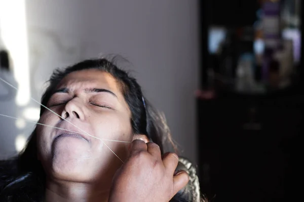 painful plucking and removal of upper lip hairs of a lady with threading. epilation cosmetic procedure in beauty parlour.