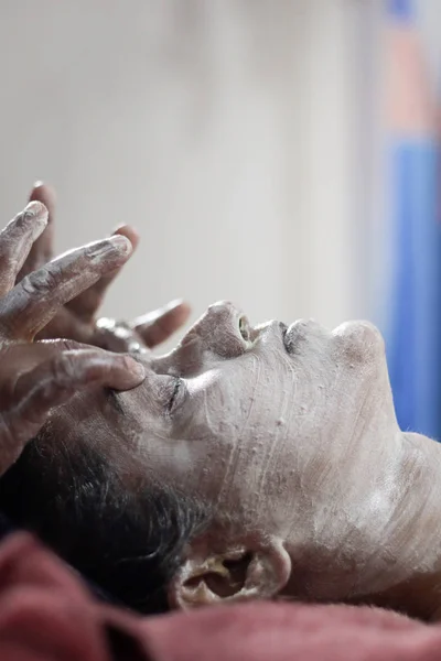 applying facial pack mask on face of a lady with hair band with eyes closed.side view