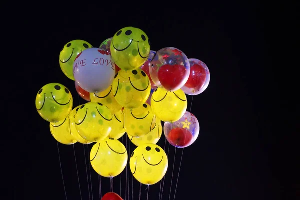 smile emoji shaped yellow balloon and heart shaped red balloons tied in bunch with threads in black background
