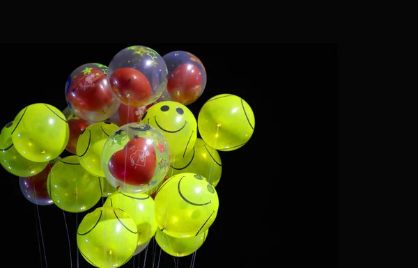 smile emoji shaped yellow balloon and heart shaped red balloons tied in bunch with threads in black background