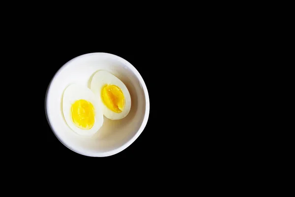 Ovo cozido cortado ao meio em uma tigela branca em fundo preto com espaço para texto — Fotografia de Stock