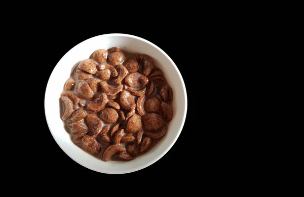 Chocolate cornflakes dipped in chocolate milk in a white bowl in black background — Stock Photo, Image