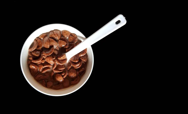 Шоколадные хлопья, смоченные в шоколадном молоке в белой миске с ложкой на черном фоне — стоковое фото