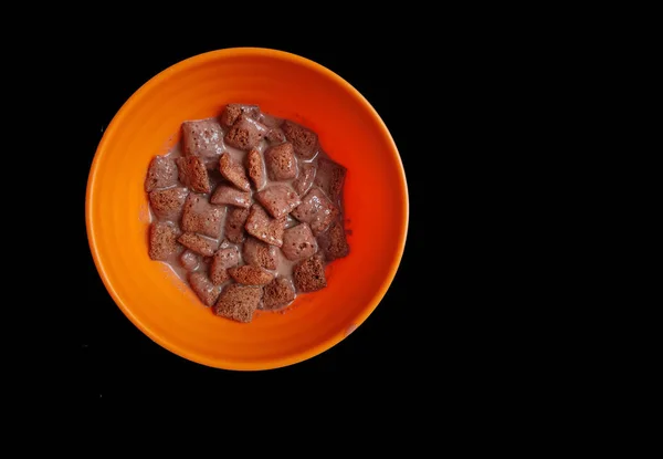 Flocons de maïs au chocolat trempés dans du lait au chocolat dans un bol blanc en fond noir — Photo