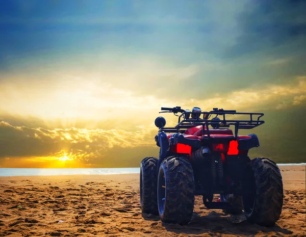 four wheeler dirt bike on sand of sea beach during sunrise with dramatic colourful sky