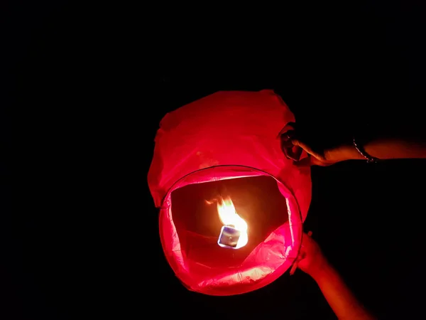 sky lantern lighting by a pair of hands holding the paper hot air balloon in a black background