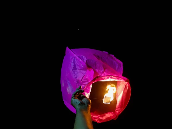 Éclairage lanterne ciel par une paire de mains tenant le ballon d'air chaud en papier dans un fond noir — Photo