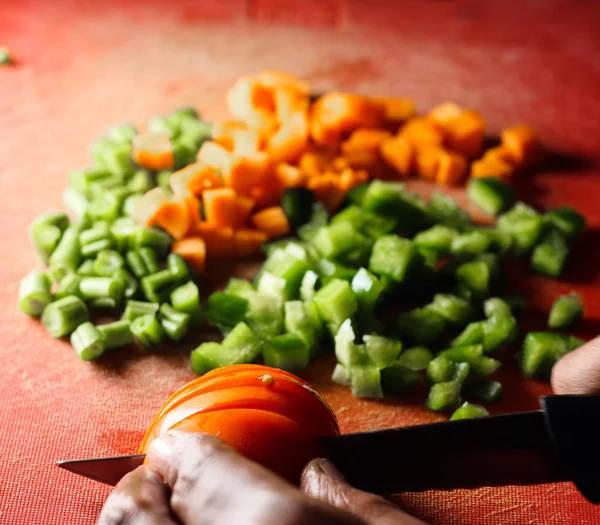 capsicum tomatoes and carrot cut into small pieces,finely chopped vegetables on a chopping board by knife in hand