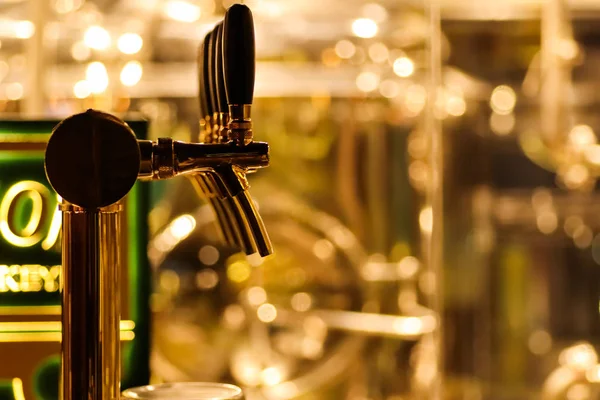 beer taps to dispense beer in mug with selective focus and distillery in background of a brewery