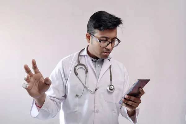 Médecin indien masculin en manteau blanc et stéthoscope dans l'expression inquiète tout en regardant le téléphone intelligent — Photo