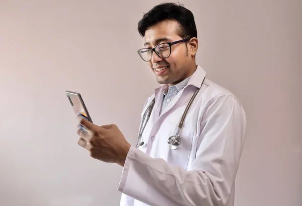 Indischer Arzt in weißem Mantel und Stethoskop berührt Smartphone Stockbild