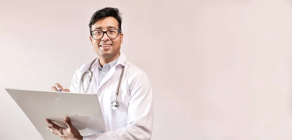 Чоловічий індійський лікар у білому пальто та стетоскоп пишуть нотатки та прописують медицину — стокове фото