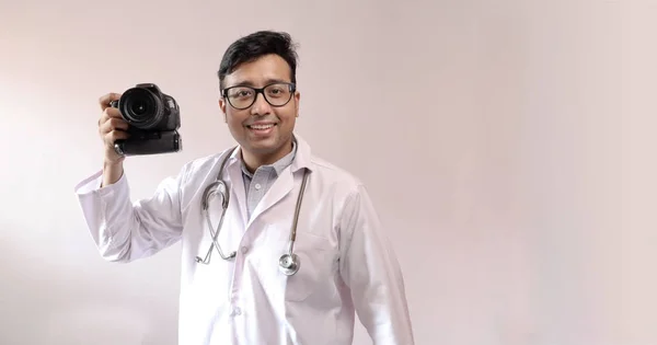 Индийский врач в белом халате и стетоскопе с камерой DSLR в руке, врач в качестве фотографа — стоковое фото