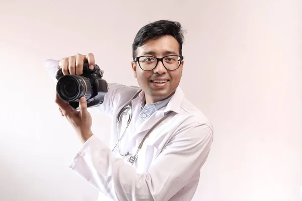 Doctor indio masculino en bata blanca y estetoscopio y una cámara réflex digital en la mano, doctor como fotógrafo —  Fotos de Stock