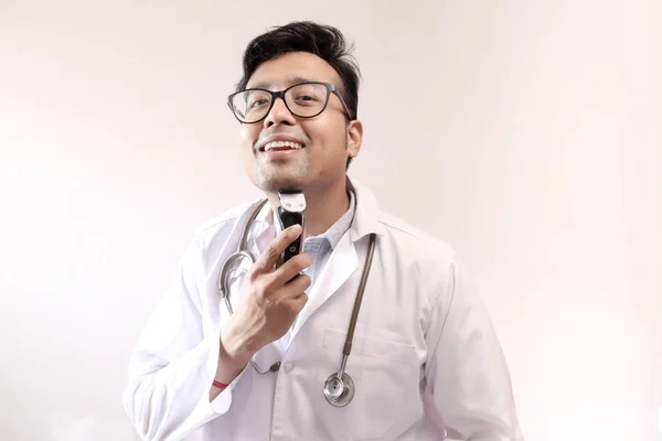 Manlig indisk doktor i vit kappa och stetoskop trimning skägg med trimmer. Doctor styling tema bild — Stockfoto