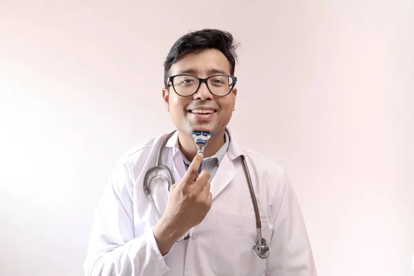 Αρσενικό ινδικό γιατρό με λευκό παλτό και στηθοσκόπιο ξυρίσματος με ξυράφι. γιατρός στυλ θέμα εικόνα — Φωτογραφία Αρχείου