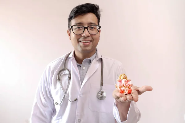 Manlig indisk doktor i vitt päls och stetoskop med en staty av Lord Ganesha i hand, Doktor tro på Gud bild — Stockfoto