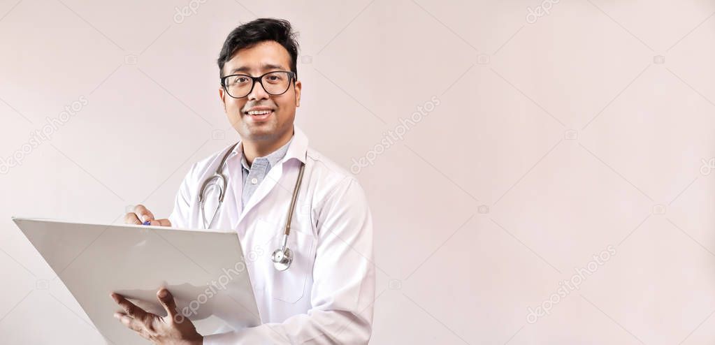 male indian doctor in white coat and stethoscope writing notes and prescribing medicine