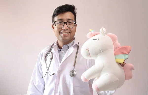 Чоловічий індійський лікар у білому пальто та стетоскоп та іграшка єдиноріг — стокове фото