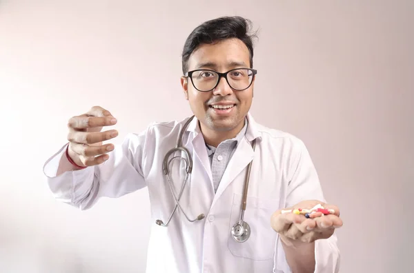 Médico indiano macho em casaco branco e estetoscópio com comprimidos de medicamentos comprimidos cápsulas na mão e mostrando sinal de dinheiro — Fotografia de Stock