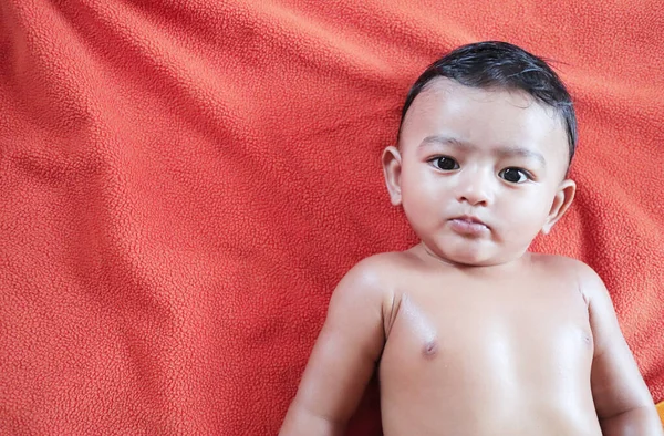 Seorang bayi laki-laki India berbaring di handuk oranye setelah dipijat minyak dan melihat kamera — Stok Foto