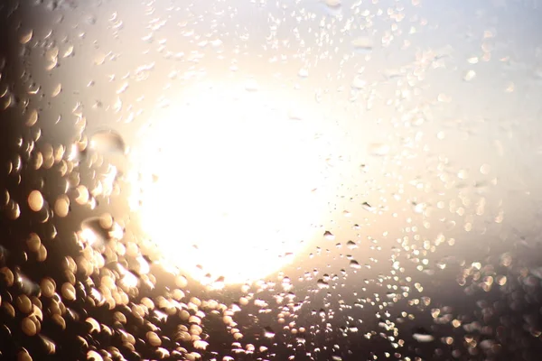 Macro photography of rain drops on the glass on a blurry background of the setting sun. Texture in dark and orange tones.