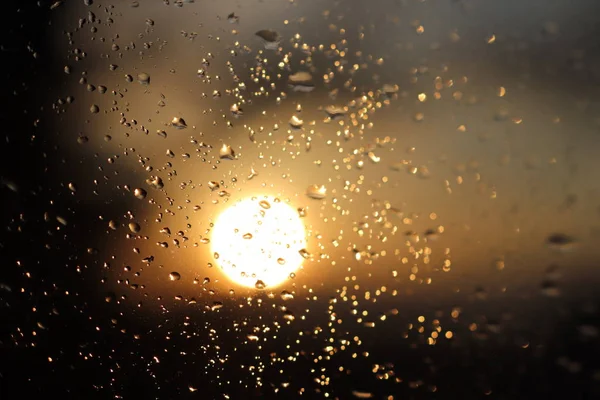 Macro photography of rain drops on the glass on a blurry background of the setting sun. Texture in dark and orange tones.