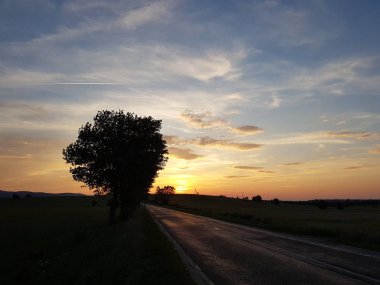 Turuncu günbatımı atmosferinde asfalt yol. Doğa ve romantik ruh güzelliği. Seyahat ederken güzel sahne. Sanatsal fotoğraf.