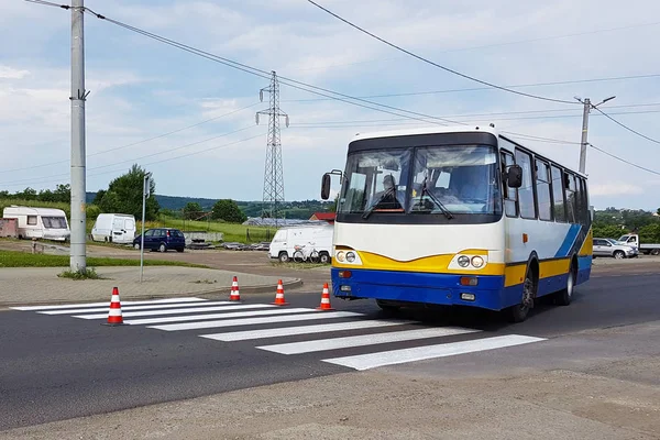 Passenger bus rides on a freshly decorated pedestrian crossing with a still not dried out red. Restriction of traffic by road signs. Update road pedestrian markings. Luminescent paint on gray asphalt.