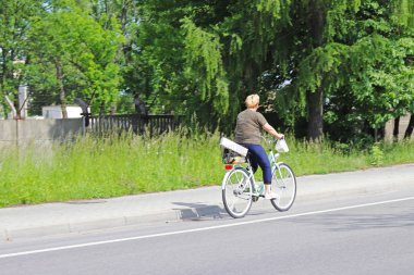 Bir kadın güneşli, açık bir günde yeşil ağaçlar çerçevede bir karayolu kenarında bir bisiklet ile gidiyor. Alternatif Masow günlük aktarım türünü. Sağlıklı ve atletik bir yaşam tarzıdır. Ekolojik 