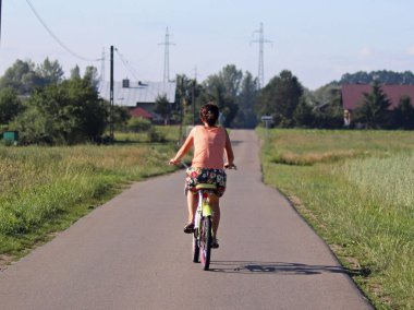 Bir futbol sahası zemin karşı köydeki bir bisiklet asfalt yolda arka tekerlek üzerinde kız rides. Ulaşım ekolojik modu. Bir genç zaman harcıyor. Sağlıklı ve aktif yaşam.