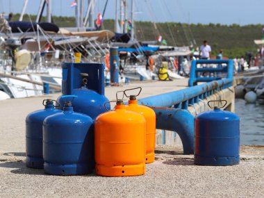 Tourist gas cylinders Stand on the pier in the marina against the backdrop of sailing yachts. Preparations for a charter cruise. Camp tanks under pressure. Energy is pumped from petroleum products. clipart