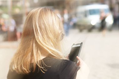 Genç güzel sarışın kız eski şehrin sokakta bir smartphone cep telefonu ile iletişim kurar. Günlük iletişimde becerikli alet. Yeni teknolojiler, modern toplumun iletişimde. Bir öğrenci olarak tarihi yerler.