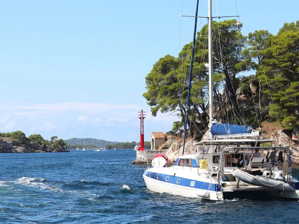 Sailing catamaran sails along the rocky green coast past the red literary sign - the fairway lighthouse. City of Sibenik in the Dalmatia region in Croatia. Adriatic sea in the Mediterranean area.