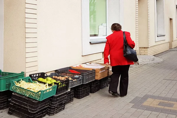 一个穿红大衣的妇女选择在街上杂货店门口的盒子里摆放的蔬菜 收割田地和果园 做饭和购物 小镇大街上的集市 — 图库照片