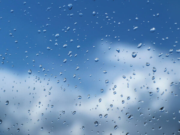 Raindrops on the glass against the blue sky with clouds.Clear blue sky with cumulus and cirrus clouds. Sunny weather. Joyful mood. High pressure. Clean air ecology. Water in a gaseous state. 