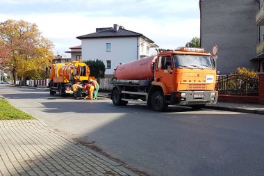 Yaslo, Polonya - 9 9 2018: Kanalizasyon temizleme özel teknik araçlarla küçük bir Avrupa kasaba sokaklarında. Turuncu arabalar ve belediye çalışanları enkaz ve kir şehirden temiz. Altyapı.