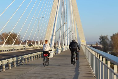 Rzeszow, Polonya - 9 9 2018: Güneşli, açık bir günde Wislok nehrin bir süspansiyon yolu Köprüsü üzerinde bisiklet sürme bir kız ile bir adam. Avrupa'nın metal konstrüksiyon teknolojik yapısı.